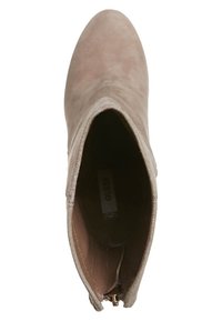 Botín de cuero suedo beige hasta el tobillo con punta redondeada, textura suave y cremallera lateral. En el interior presenta un forro marrón claro con una etiqueta de la marca.
