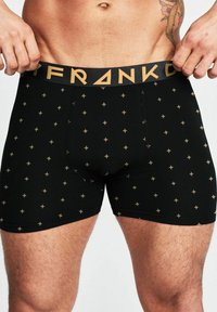 Svarta boxershorts med ett mönster av guldstjärnor, elastisk midja med "FRANK" i svart och guld, tillverkade av ett slätt, stretchigt material.