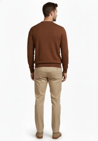 Jersey tejido marrón con un patrón texturizado, con un cuello en contraste. Pantalones beige con bolsillos traseros y zapatos marrones claros.