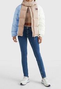 Puchowa kurtka z kolorowym blokiem w odcieniach niebieskiego, beżowego i białego, zapinana na zamek, z kapturem. Zestawiona z ciemnoniebieskimi dżinsami i trampkami.