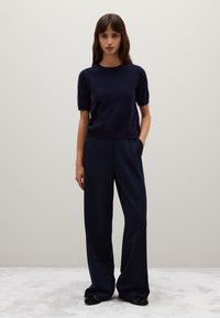 Maglione navy a maniche corte abbinato a pantaloni navy a gamba larga e scarpe slip-on nere decorate; tessuto morbido, vestibilità rilassata.