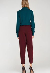 Turkusowa koszula z długim rękawem i kołnierzykiem, w zestawieniu z bordowymi spodniami w kant. Ubranie zdobione jest guzikami i ma gładką fakturę.