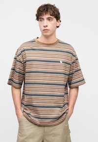 Ριγέ μπλουζάκι σε καφέ, μπεζ και ναυτικό μπλε. Κοντά μανίκια, στρογγυλή λαιμόκοψη, υφασμάτινο μείγμα βαμβακιού. Διαθέτει μικρό λογότυπο στο στήθος.