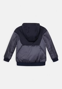 Marinblå huvjacka med quiltat mönster, elastiska ärmslut och en slät yta. Lätt mörkare paneler skapar en lager-effekt.