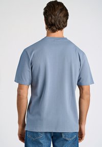 Jasnoniebieska koszulka z krótkim rękawem i okrągłym dekoltem, wykonana z miękkiego materiału. Charakteryzuje się luźnym krojem i jest zestawiona z dżinsami.