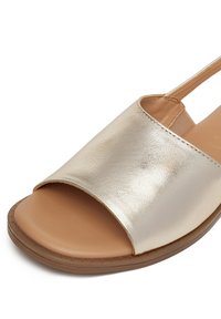 Zlaté metalické kožené sandály s otevřenou špičkou a designem s páskem na patě. Texturovaná béžová stélka a flexibilní hnědá gumová podešev.