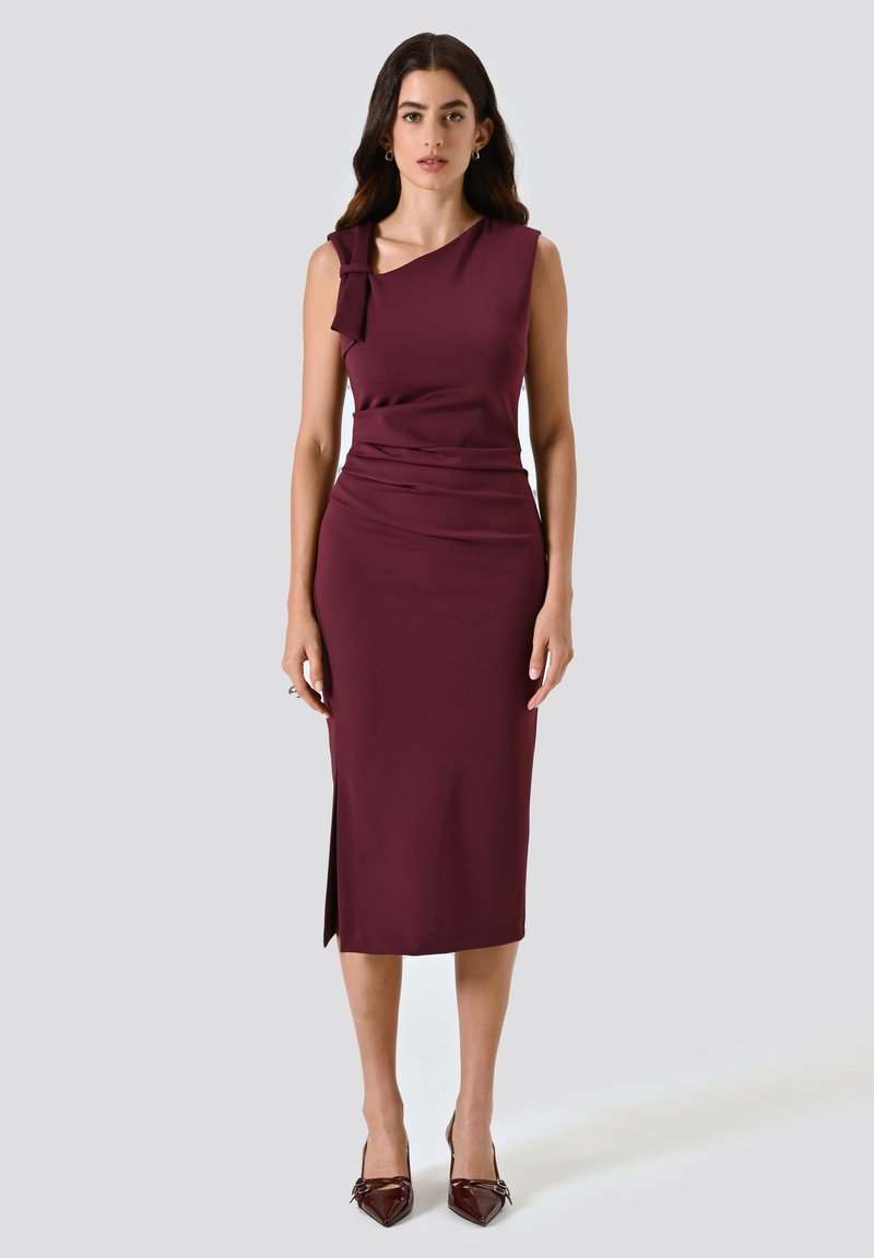 Burgunderfarbenes Midi-Kleid mit einem schulterfreien Design, das mit einer Schleifendetail versehen ist. Glattes Material, seitlicher Schlitz und taillierte Silhouette. Sichtbare Stilettos.