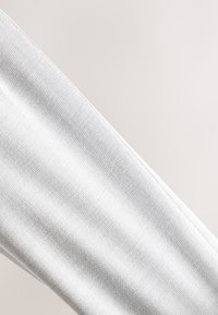 Gros plan sur un tissu blanc texturé avec des coutures visibles le long d'une couture diagonale.