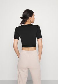 T-shirt nera corta con maniche corte e banda logo a tonalità sull'orlo, abbinata a pantaloni da jogging beige chiaro con cintura elastica.