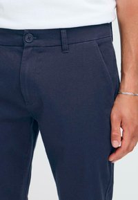 Marineblå, slim-fit bukser med en glat tekstur, enkelt knaplukning, sidelommer og et rent taljebånddesign.