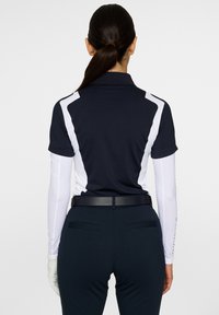 Marinblå pikétröja med vita sidopaneler, korta ärmar och krage. Matcher med mörka byxor och ett svart bälte, med praktiska bakfickor.