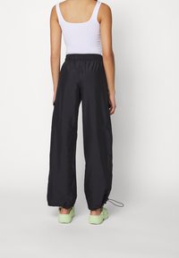 Zwarte wijde broek met een elastische tailleband, gemaakt van lichtgewicht materiaal, met trekkoorden aan de onderkant en zijzakken.