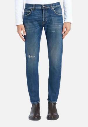 Blå slim-fit jeans med let slid, båret med mørkebrune ankelstøvler og en hvid bluse med lange ærmer.