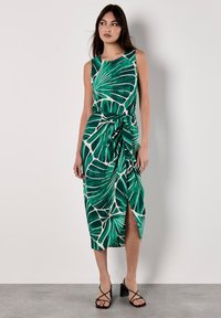 Grünes Kleid mit Blättermuster, ärmelloses Design, gebundener Taillendetail, knielang mit Schlitz, aus einem fließenden Stoff.
