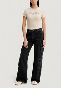 Béžové přiléhavé tričko s logem "Tommy Jeans", doplněné černými cargo kalhotami s velkými bočními kapsami a volným střihem.
