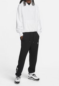 Witte hoodie met een zak, zwarte joggingbroek met strepen aan de zijkant en zwart-witte sneakers. Heeft Nike-logo's en een losse pasvorm.