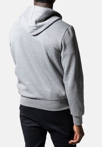 Sudadera gris con una textura suave, que presenta una capucha con cordón, puños y dobladillo acanalados. El diseño es simple y casual, adecuado para el uso diario.
