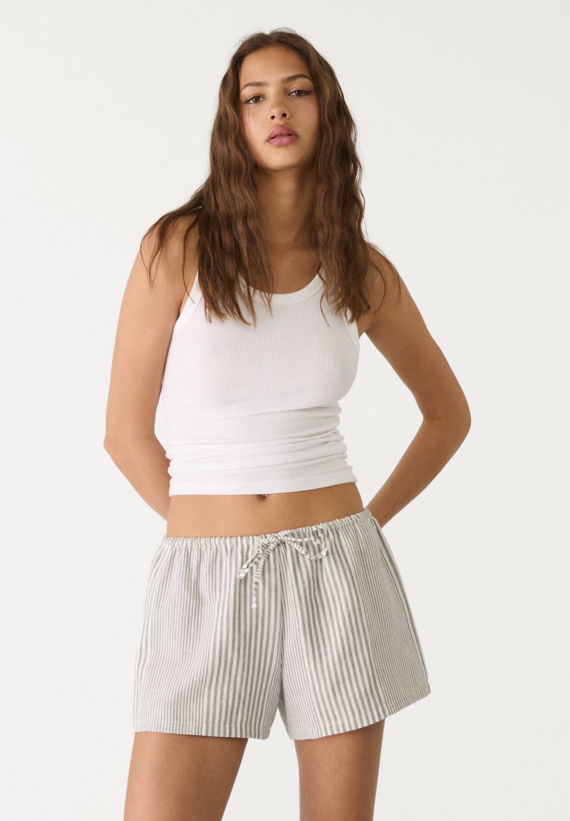 Vit ribbad linne med grårandiga shorts med dragsko. Shortsen har en elastisk midja och en avslappnad passform. Slät bomullstextur.