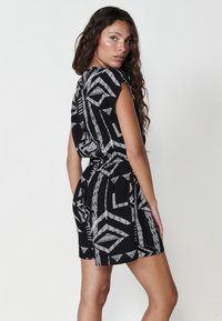 Zwarte korte jurk met een wit geometrisch patroon, voorzien van cap sleeves, een getailleerde taille en een comfortabele pasvorm. Zachte stoftextuur.