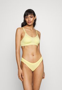 Geel naadloze bralette met verstelbare bandjes en bijpassende low-rise thong. Lichtgewicht stof met een gladde textuur. Eenvoudig, minimalistisch ontwerp.