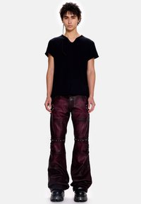 Μαύρο κοντομάνικο πουκάμισο σε συνδυασμό με σκούρα κόκκινα δερμάτινα παντελόνια με ασημένιες λεπτομέρειες με τρουκ και φαρδιά τελειώματα. Μαύρα παπούτσια ολοκληρώνουν την εμφάνιση.