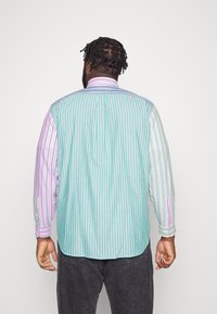 Camisa de manga larga con rayas verticales alternadas en verde, morado y blanco. Material de algodón, con cuello y puños abotonados.