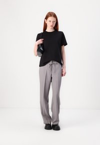 Sort kortærmet T-shirt, grå skræddersyede bukser med snøre og sorte chunky sko. Enkel, ren design med en neutral farvepalet.