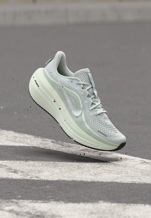 Chaussure de course Nike gris clair avec semelle amortie en suspension au-dessus d'un passage piéton sur l'asphalte, avec de petites particules de saleté sous la semelle.