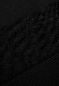 Zbliżenie czarnego materiału z trzema wyraźnie widocznymi fakturowanymi wzorami splotu, ułożonymi w sposób diagonalny.