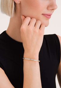 Bracciale in argento con accenti di cristallo trasparente, caratterizzato da un design elegante e minimalista. La superficie ha una texture lucida e liscia.