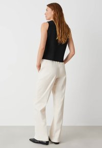 Zwarte mouwloze top met een relaxte pasvorm, gecombineerd met crèmekleurige, hoge taille wijde broek en zwarte puntige ballerina's, tegen een neutrale achtergrond.