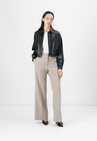 Giacca cropped in ecopelle nera, maglietta bianca a girocollo, pantaloni larghi di un beige chiaro e décolleté neri a punta. Design semplice, texture morbida.