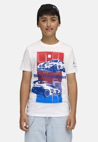 Balta kokvilnas T-krekls ar ziliem un sarkaniem BMW M Motorsport automašīnu grafikiem, īsām piedurknēm, apaļu kakla izgriezumu un nelielu BMW logo uz piedurknes.