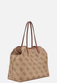 Beżowa torba tote z brązowym wzorem monogramu, z dwiema brązowymi skórzanymi uchwytami i miękkim materiałem. Zdefiniowany kształt z widocznymi detalami szwów.