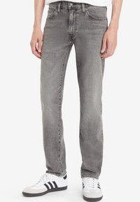 Jeans in denim grigio con taglio dritto, design a cinque tasche e finitura sbiadita. Abbinati a scarpe sportive bianche e nere.