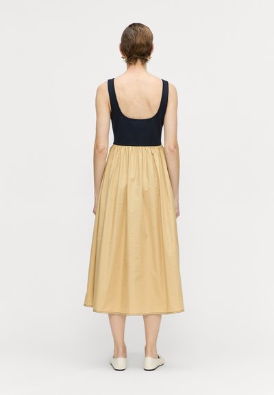Ein ärmelloses Kleid mit einem marineblauen Oberteil und einem fließenden, beigen Rock. Glatte Stofftextur mit lockerer Passform und knöchellangem Design.