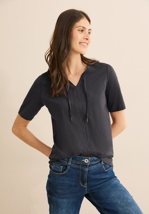 Donker marineblauw T-shirt met korte mouwen en een V-hals, met trekkoordaccenten en een subtiele textuur; gecombineerd met bl blauwe denim jeans met contrasterende stiksels.