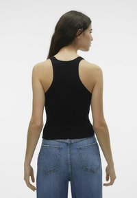 Mustmustriibuline tank top, millel on kehaümberümpav lõige ja sportlik seljaosa, kombineeritud helesiniste kõrge vöökohaga teksadega, millel on tagakotid.