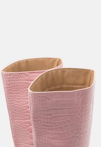 Une paire de bottes en cuir rose avec un motif crocodile et une doublure en daim beige, montrées de dessus sur un fond blanc.