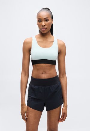 Helesinine spordirinnahoidja musta paelaga koos mustade sportlike lühikestega. Sile tekstuur, keha lähenev disain ja lihtsad aktsendid.