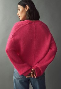 Pulover pufos roz, cu mâneci largi și o croială lejeră, purtat cu blugi blue. Prezintă un design simplu și un material texturat.