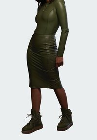 Olivgrünes, tailliertes Kleid mit langen Ärmeln und Midi-Länge. Kombiniert mit braunen High-Top-Sneakern mit Schnürung und strukturiertem Äußeren.