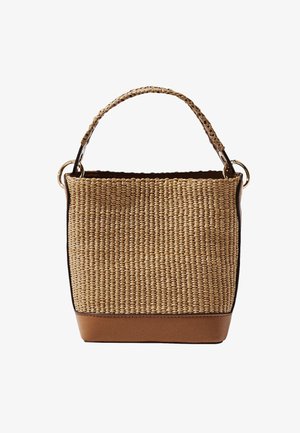 Prostokątna torebka ze słomy o splatanej strukturze, z plecionym uchwytem i brązową skórzaną podstawą oraz wykończeniem, złote pierścienie mocujące na białym tle.