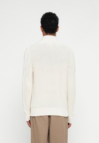 Jersey blanco de cuello redondo con detalles de punto de cable texturizado a lo largo de las mangas y puños acanalados; corte relajado.