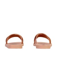Et par lyserøde flade sandaler med en enkelt bølget rem set forfra mod en hvid baggrund.