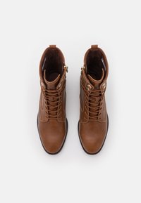 Braune Leder-Stiefeletten mit Schnürsenkeln und seitlichen Reißverschlüssen, mit einer glatten Oberfläche und strukturiertem Innenfutter, abgerundeter Zehenpartie und minimalistischem Design.