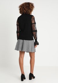 Czarny sweter z koronkowymi długimi rękawami, zestawiony z w kratę czarno-białą spódnicą. Czarne szpilki uzupełniają strój.