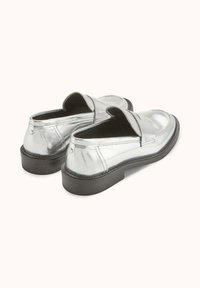 Mocassins métalliques argentés avec une semelle en caoutchouc noir et un bout arrondi, présentant une texture lisse et des accents de coutures minimalistes.