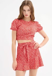 Top corto rojo con flores y mangas abullonadas, acompañado de una falda acampanada a juego con un lazo en la cintura. Tela suave con un pequeño y delicado patrón blanco.
