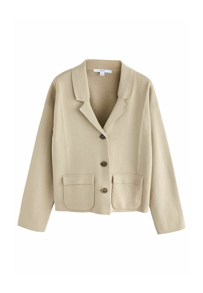 Béžový blazer s dlouhým rukávem, s vykrojeným límcem, dvěma předními kapsami a čtyřmi tmavými knoflíky. Textura vypadá tkaná nebo pletená.